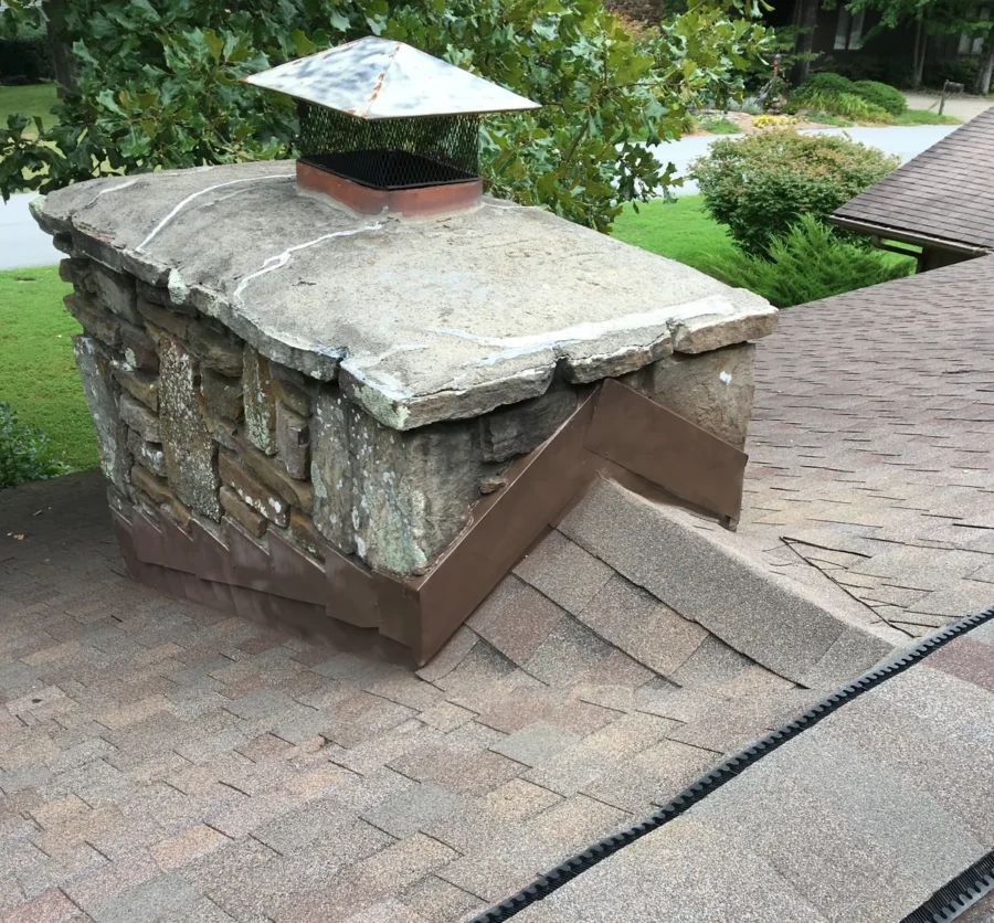 Finished chimney flashing repair by Foster Roofing, with a new metal cricket behind a stone chimney on an asphalt shingle roof
